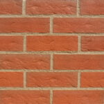 A display panel image of bricks laid in stagger bond. The brick slips are a mid red, roll textured and sanded finish. The bricks are pointed in a mid sandstone mortar