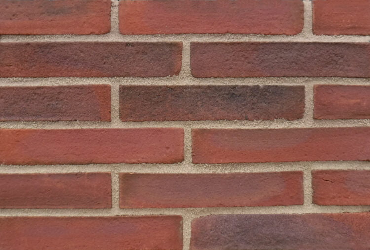 A display panel of roman length brick slips. The bricks are longer than normal bricks, laid in a third stagger bond and pointed with a sand and cement pointing mortar. The bricks have a sand finish and are a blend of red and brown tones.