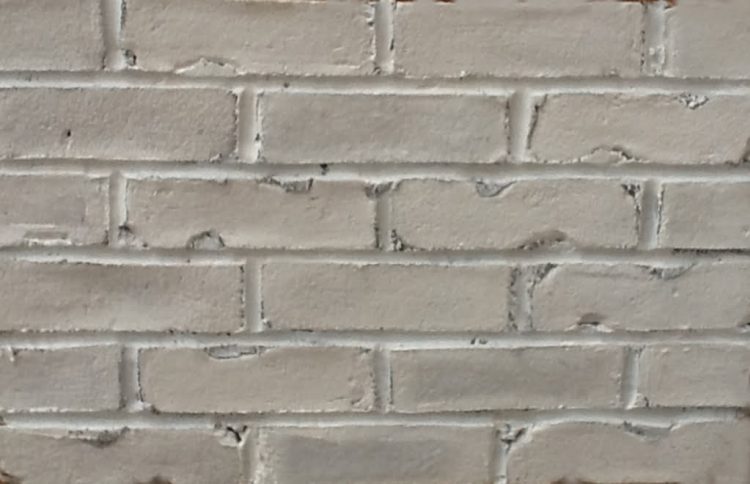 Rustic brick slips are stuck on a panel and pointed using grey mortar. The bricks have an uneven surface and distorted edges. The panel has been painted completely white.