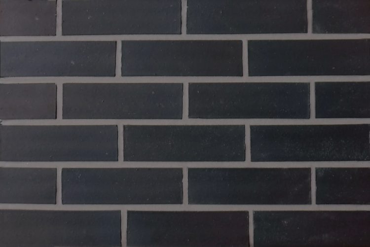 A black smooth brick slip panel. The edges of the brick are straight and square and the mortar is a mid grey